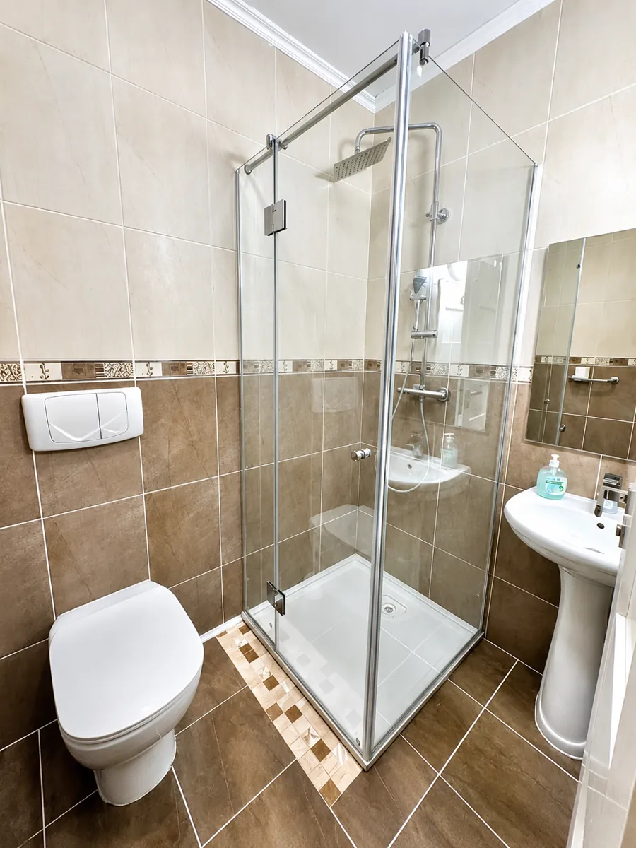 Private bathroom with a glass corner shower, basin and tiled walls