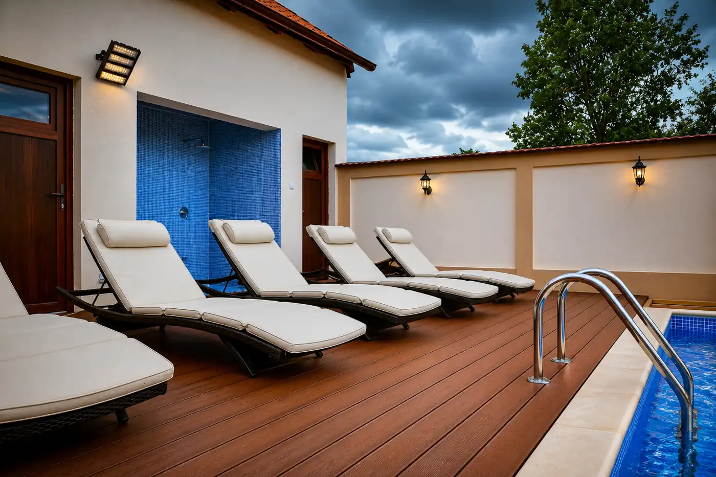 Cushioned loungers on the wooden pool deck beside the open-air shower at dusk