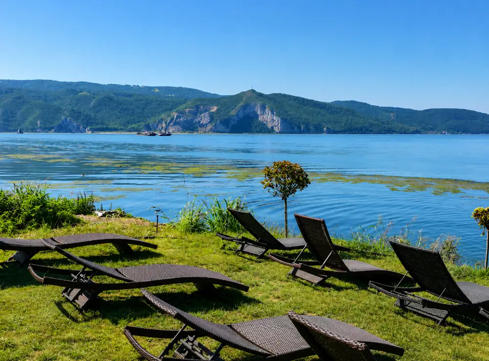 Sun loungers on the grass beside the Danube with the Iron Gates cliffs across the water